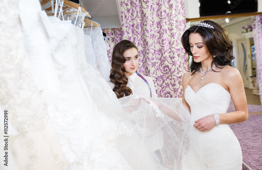 Female trying on wedding dress in a shop with women assistant.