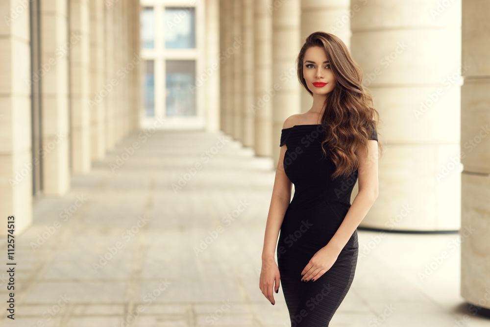 Young elegant girl posing at city street. Pretty beautiful business woman in elegant black dress against city background. - obrazy, fototapety, plakaty 