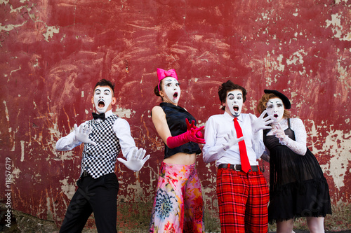 Four mimes in fear stand in the background of a red wall.