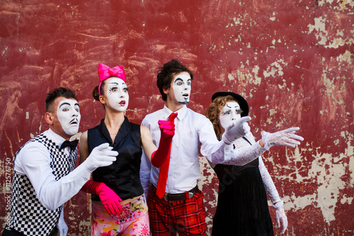 Four mimes looking aside on the background of a red wall.