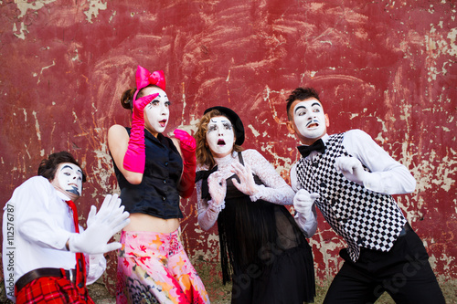 Four mimes standing in awe at the background of a red wall.