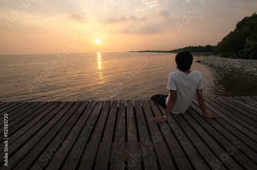 silhouette Young man relax siting on pier sea beach looks to right with sunset sky with copy space for label text or banner