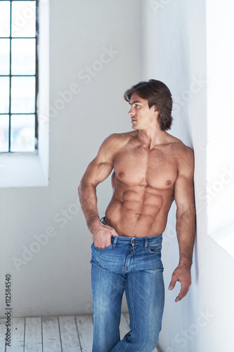 Suntanned muscular male in blue jeans posing.