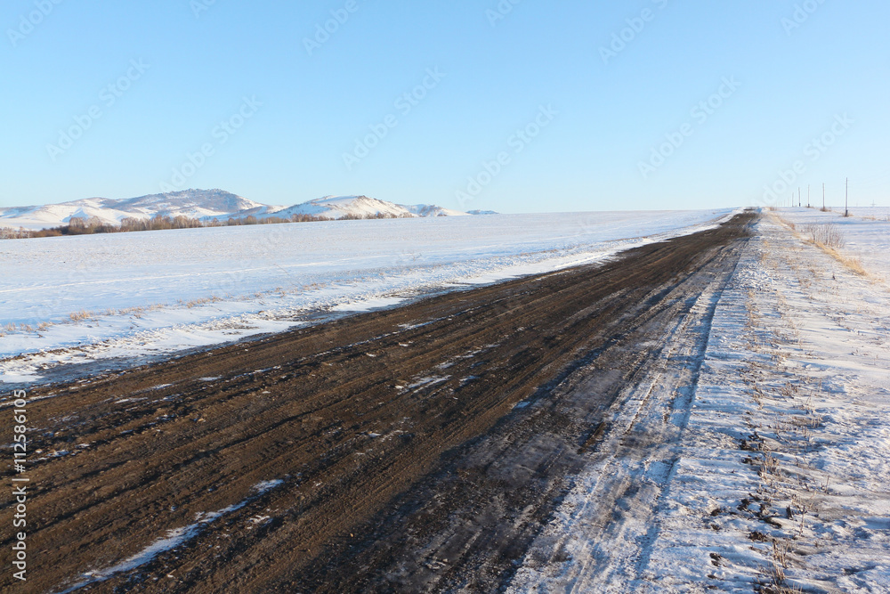 The rural unpaved road  going among snow fields
