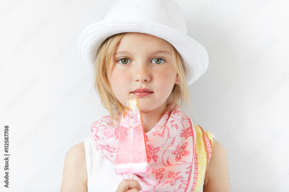 Restful little European girl with yummy popsicle posing for camera. In summer hat and nice scarf she looks like traveller enjoying her happy child life and sweets. Restful little European girl with yummy popsicle posing for camera. In summer hat and nice scarf she looks like traveller enjoying her happy child life and sweets.