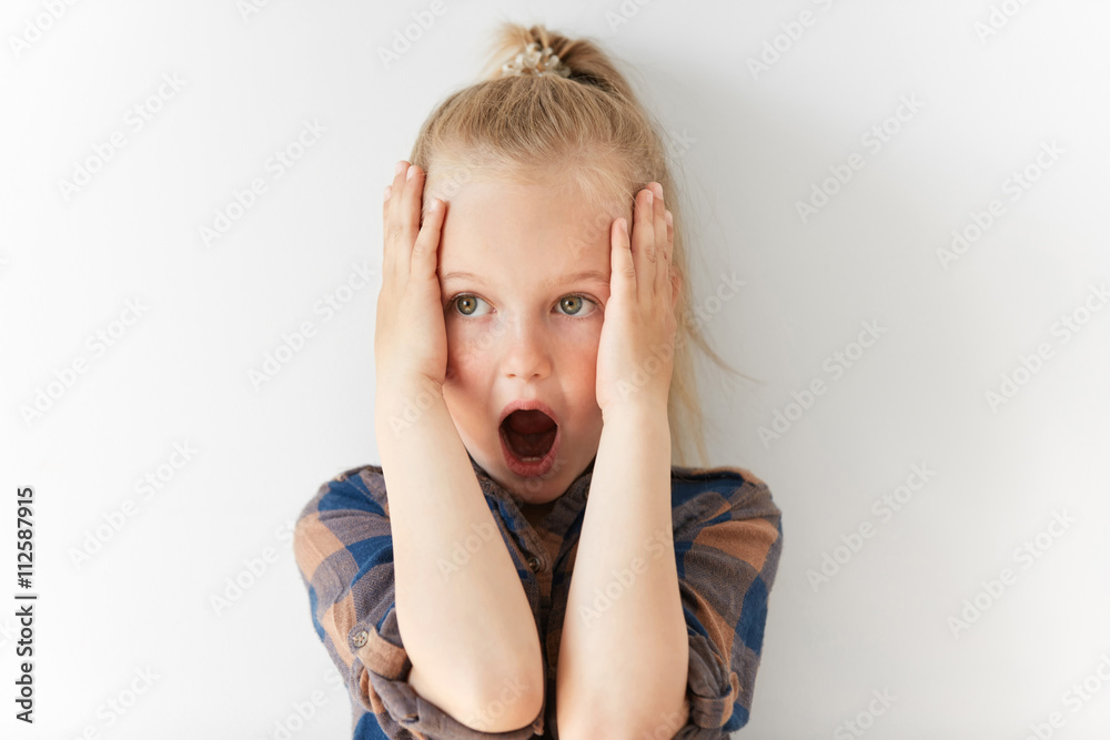 Blond Caucasian female child opening her mouth in astonishment and clutching head in horror. Scared and terrified kid is frightened by negative news and ready to scream. Blond Caucasian female child opening her mouth in astonishment and clutching head in horror. Scared and terrified kid is frightened by negative news and ready to scream.