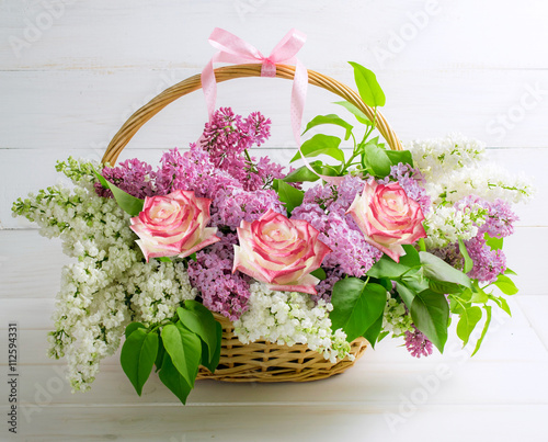 Lilac bouquet with roses in basket on background of shabby wooden boards