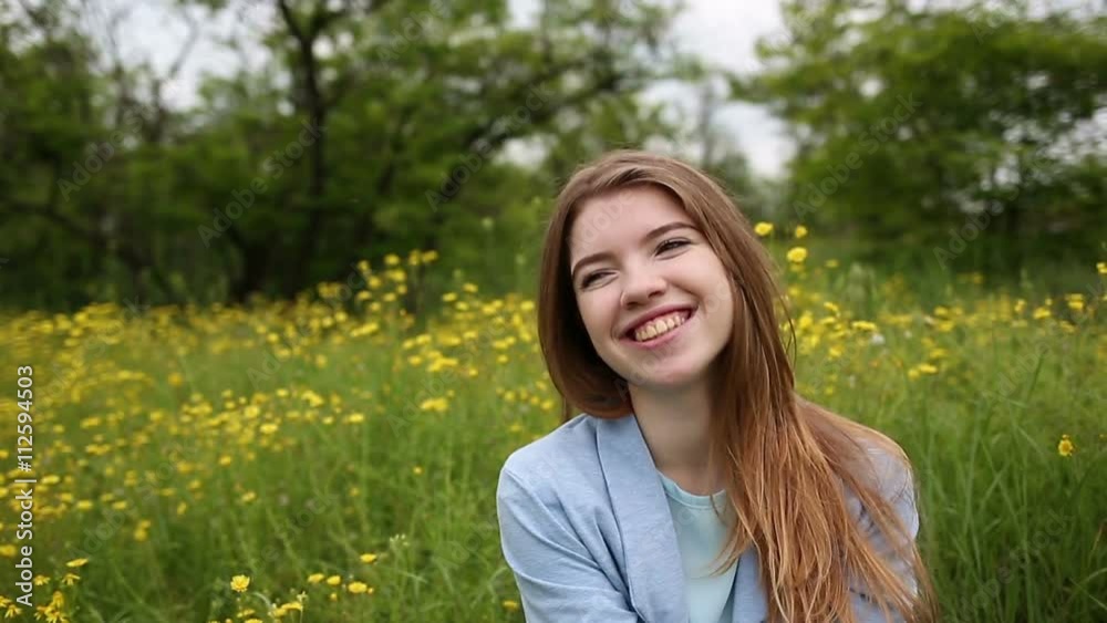 Lovely girl laughing. Girl sits on a meadow among the wildflowers. Female face close up. Lovely girl laughing. Girl sits on a meadow among the wildflowers. Female face close up.