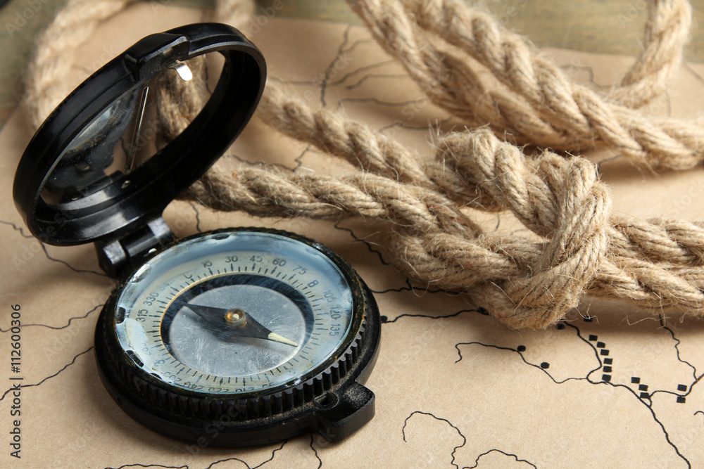 Fototapeta premium the folded rope with an open compass lying on old map