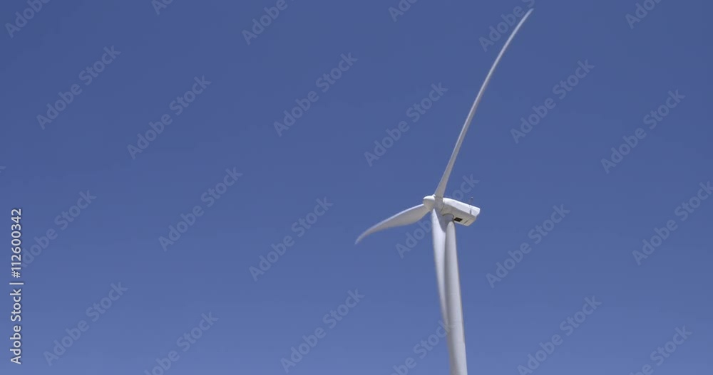 Wind turbine generating electricity rotates against a clear blue sky.  Seamlessly looping clip.  Locked off shot, originally recorded in 4K.