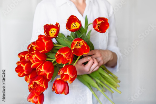 Fototapeta Naklejka Na Ścianę i Meble -  
Large beautiful bouquet of red tulips in the hands of a girl in a white shirt