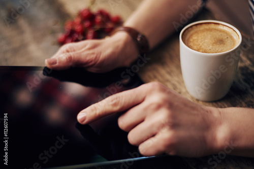 Close-up of female finger pointing at digital display of tablet pc siting at the table with coffee mug. Concept of modern electronic device and lifestyle. 