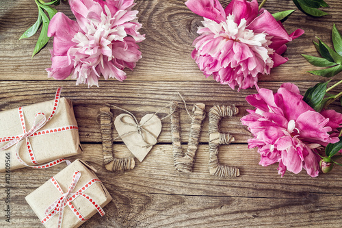 Purple peonies with letters LOVE and gift boxes on old wooden bo