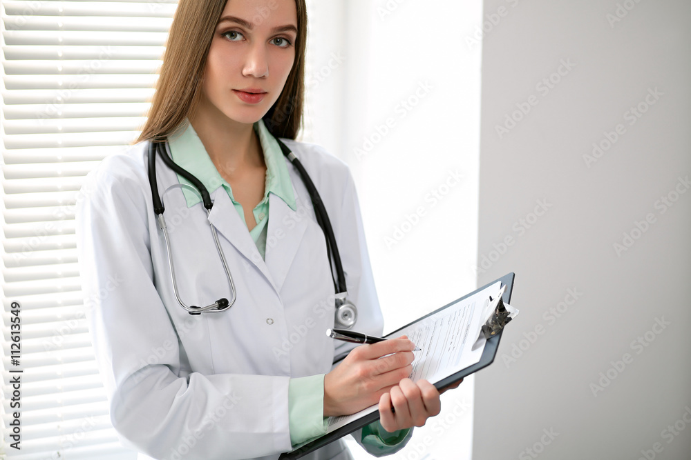 Female doctor brunette sitting at the table near the window in hospital and typing at laptop computer Female doctor brunette sitting at the table near the window in hospital and typing at laptop computer