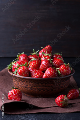 Fresh strawberry in the brown bowl on dark table