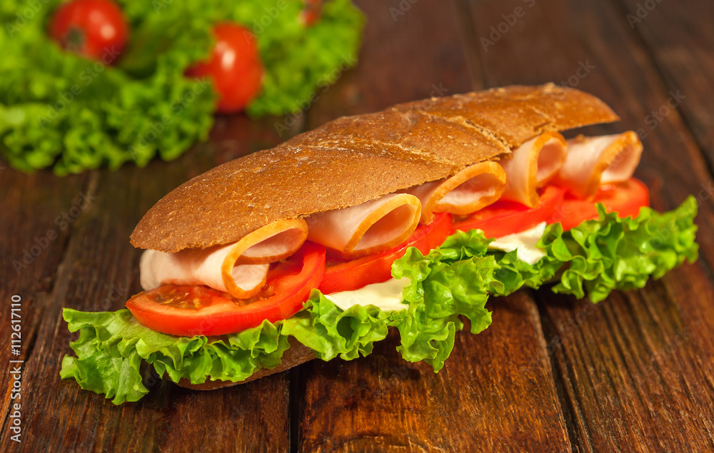 Sandwich with lettuce, tomatoes, ham, and cheese on wooden table.