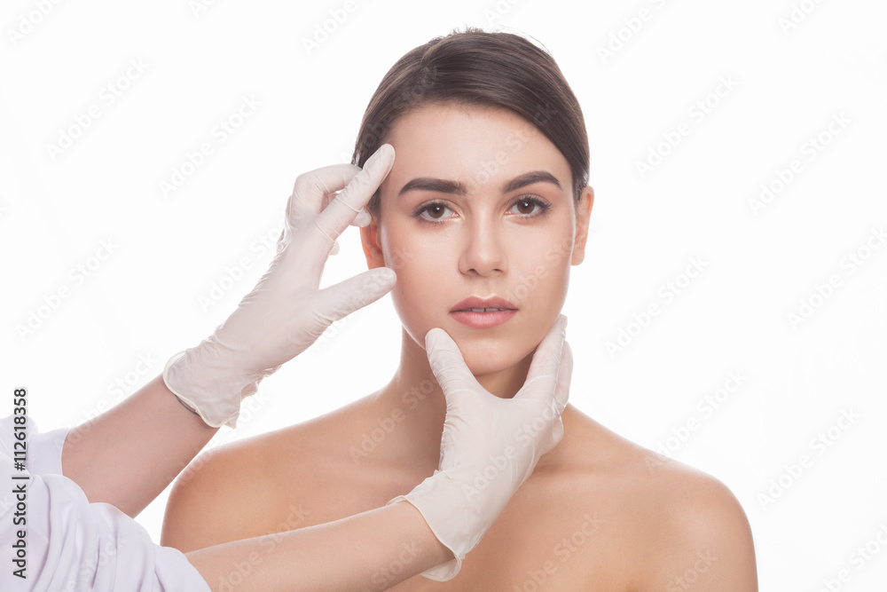 Portrait of serious lady having her face examined by professional doctor isolated over white background.