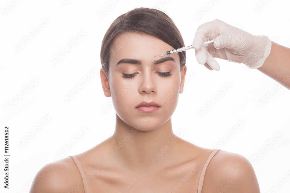 Medical injection. Portrait of beautiful young woman keeping eyes closed while doctors hands in gloves making injection in her face isolated on white.