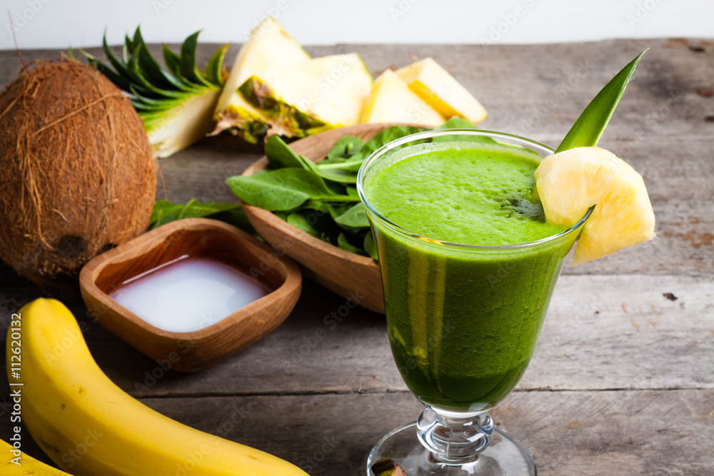 A glass of green smoothies, and the ingredients from which it was made. Smoothies with spinach, banana, coconut water, pineapple on gray wooden table.