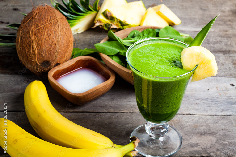 A glass of green smoothies, and the ingredients from which it was made. Smoothies with spinach, banana, coconut water, pineapple on gray wooden table.