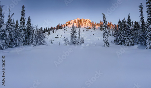 Snowy mountains on an early winter morning. Photograph was taken in South Ural, Russia. Panorama with forest, mountains, clouds and clear sky.