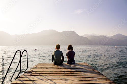 Brother and sister sitting on pier by lake photo