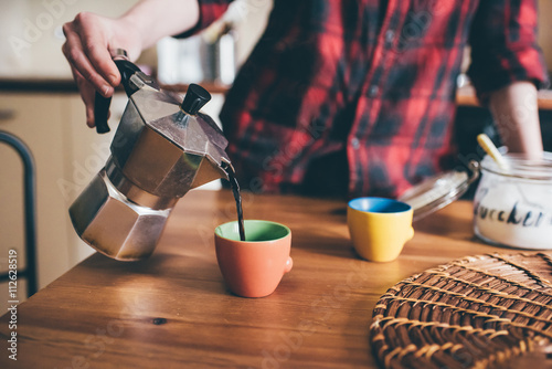 Close up of the hand of young woman pouring coffee from a moka in a cup - morning, breakfast, break concept photo