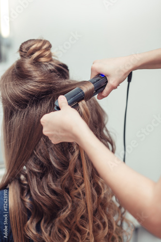 Closeup of hairdresser doing hairstyle with hair iron
