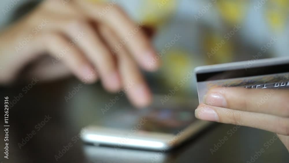 The young woman is working with the cell phone holding the debit card in the left hand and dialing the number with the right one. The young woman is working with the cell phone holding the debit card in the left hand and dialing the number with the right one.