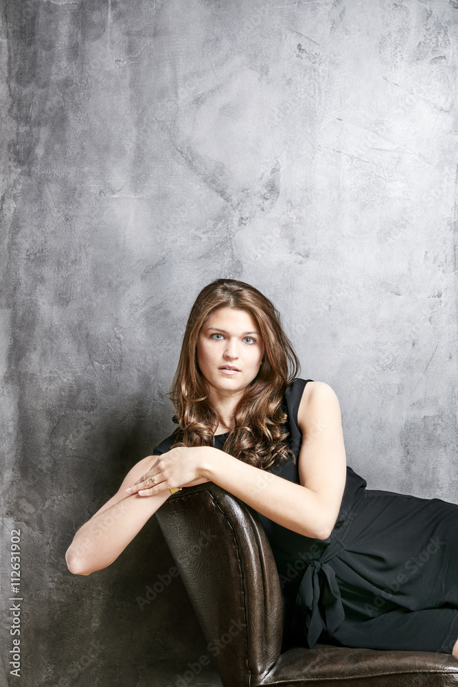 Portrait of young woman wearing black dress on leather chair Portrait of young woman wearing black dress on leather chair