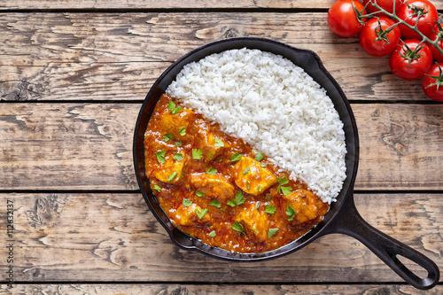 Tikka masala traditional butter chicken spicy meat food and rice with tomatoes in cast iron skillet on vintage wooden background. Karahi chicken recipe