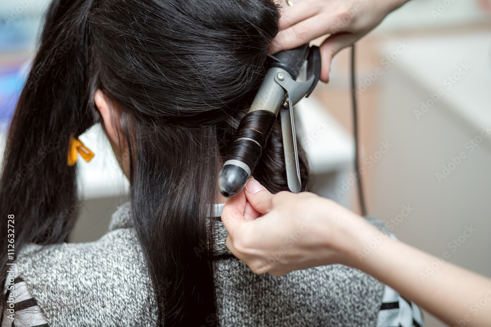 Fototapeta premium The Barber makes an Evening or wedding hairstyle with long beautiful dark hair in hairdresser salon