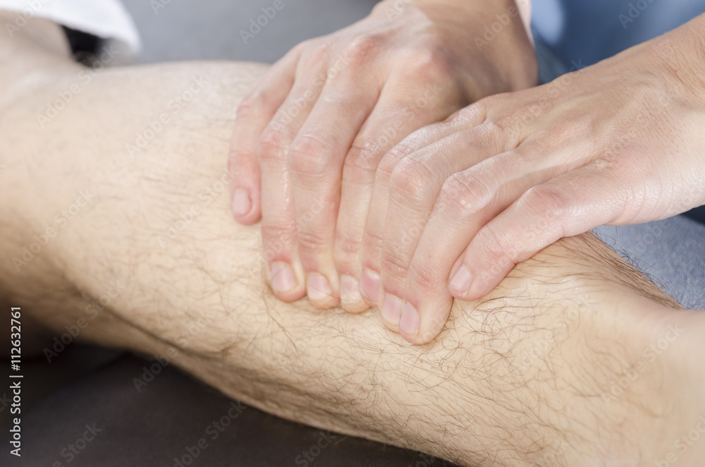 Closeup of hands of chiropractor doing calf muscle massage to ma Closeup of hands of chiropractor doing calf muscle massage to ma