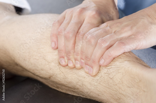 Closeup of hands of chiropractor doing calf muscle massage to ma