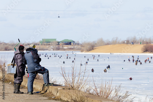 Two fishermen are looking at ice fishing on the river.