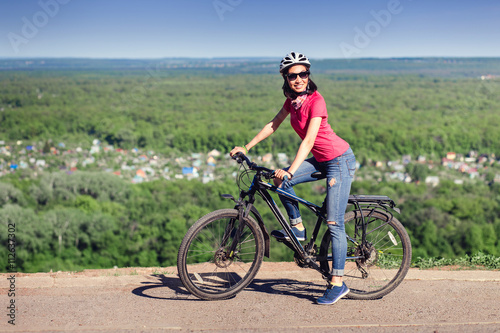 Pretty young woman on the bike at the top of the hill