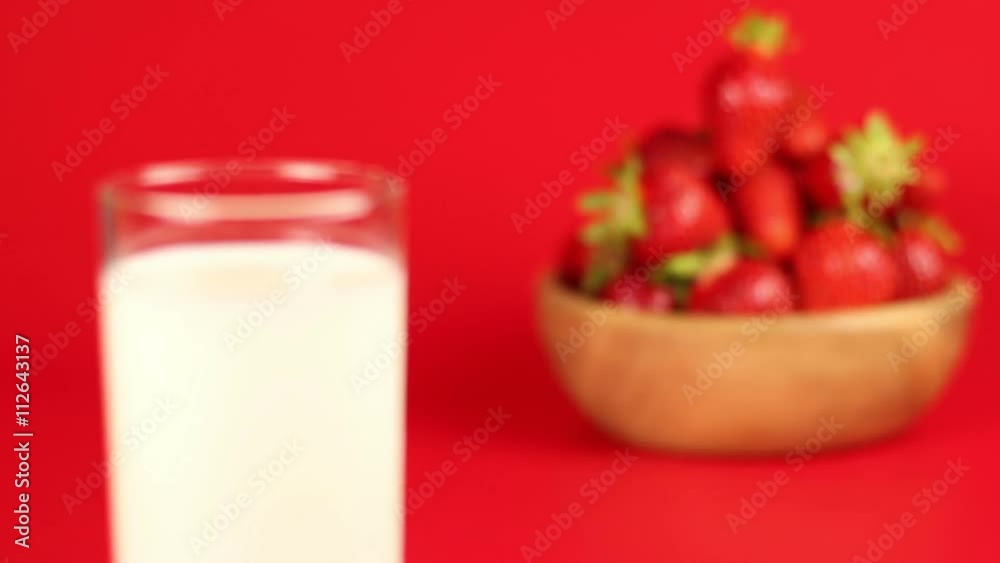 A glass of milk and red ripe strawberry in wooden bowl on red background A glass of milk and red ripe strawberry in wooden bowl on red background