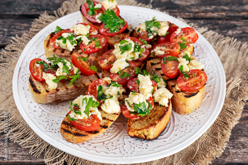Two-bite grilled appetizer bruschettas with red grape tomatoes, mozzarella and parsley sprinkle