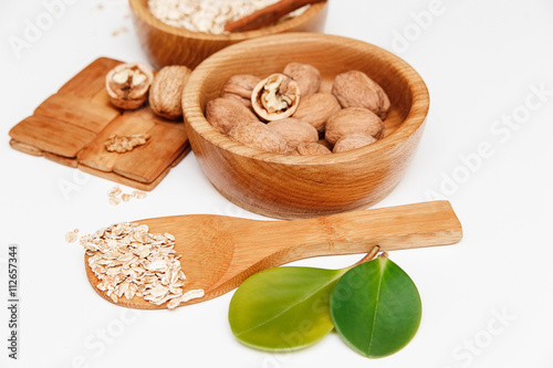 There are Walnuts and Rolled Oats in the Wooden Plates with Sticks of Cinnamon,Wooden Support,Spoon,Green Leaves,Healthy Fresh Organic Food on the White Background