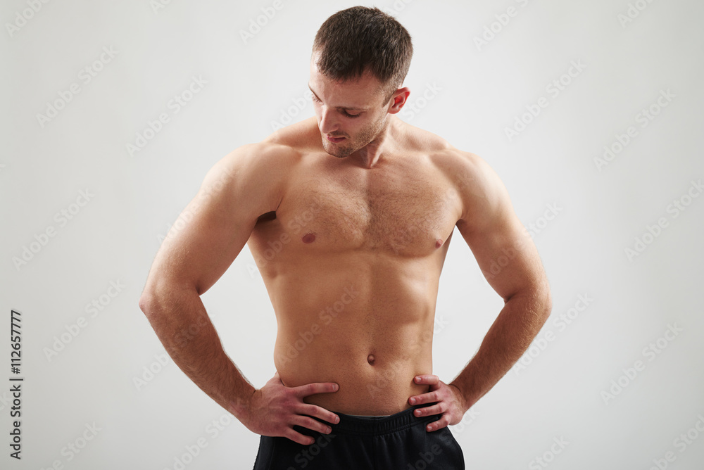 Athletic bare-chested man is looking at his right arm