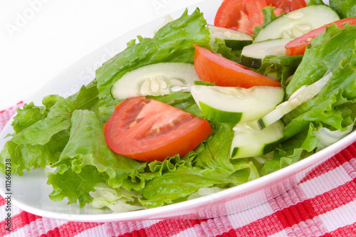 Healthy Salad with Tomatoes and Cucumbers – A plate of fresh lettuce, tomatoes and cucumbers. Red checkered placemat in background.