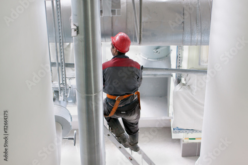 Builder repairman standing on ladder near large ventilation pipe