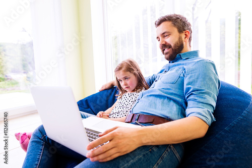 Father and daughter, playing on laptop, sitting on beanbag