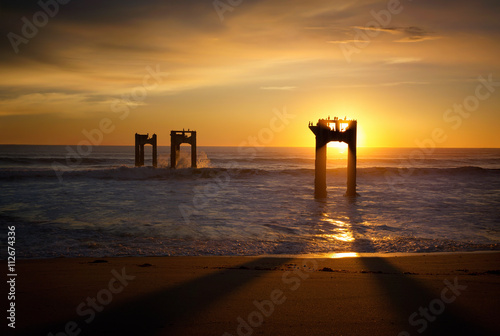 Silhouette of dilapidated pier supports in ocean at sunset  photo