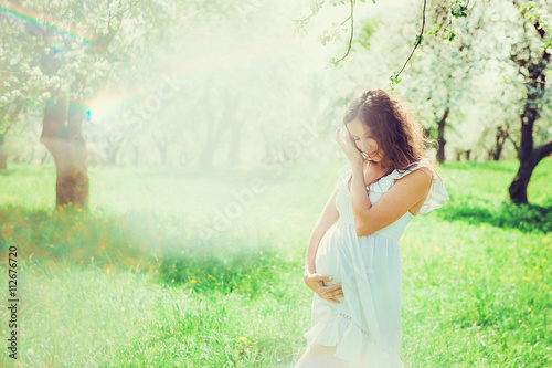 Pregnant woman in the apple orchard is holding tummy

