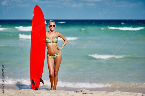 Young pretty woman holding surfboard on seaside beach - full len