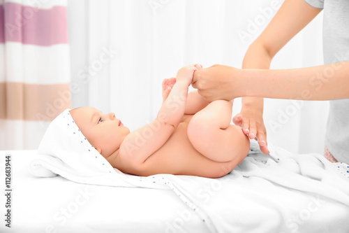 Mother hands applying cream on little baby body in room