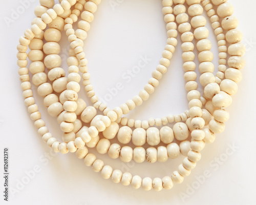 Jewelry necklace made of threads with bone beads on white background. Many strands of varying sized beads of polished ivory