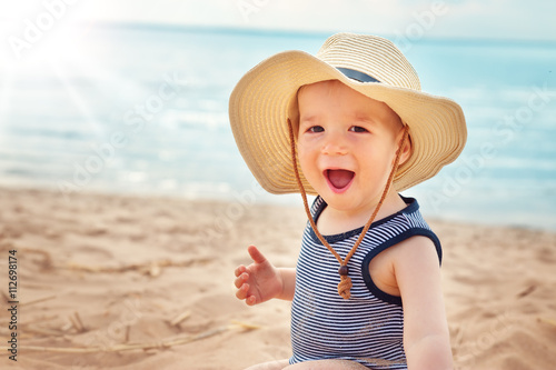 little boy sitting at the beach in straw hat