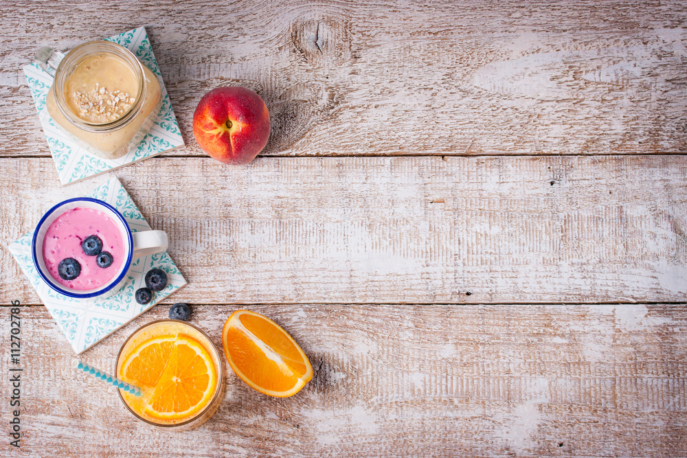 A mix of three smoothies with blueberry, orange and peach on a wooden background with copy space, top view